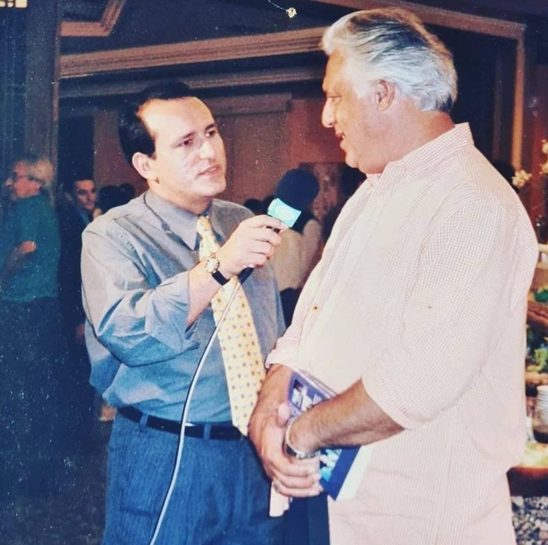 Edilásio Jr. entrevistando um ator, que segura um livro, com o microfone verde da Band